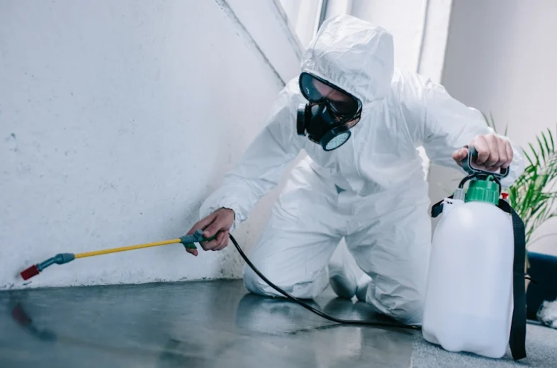 Professional Pest Control in Milwaukee in protective suit and gas mask using a sprayer near a wall.